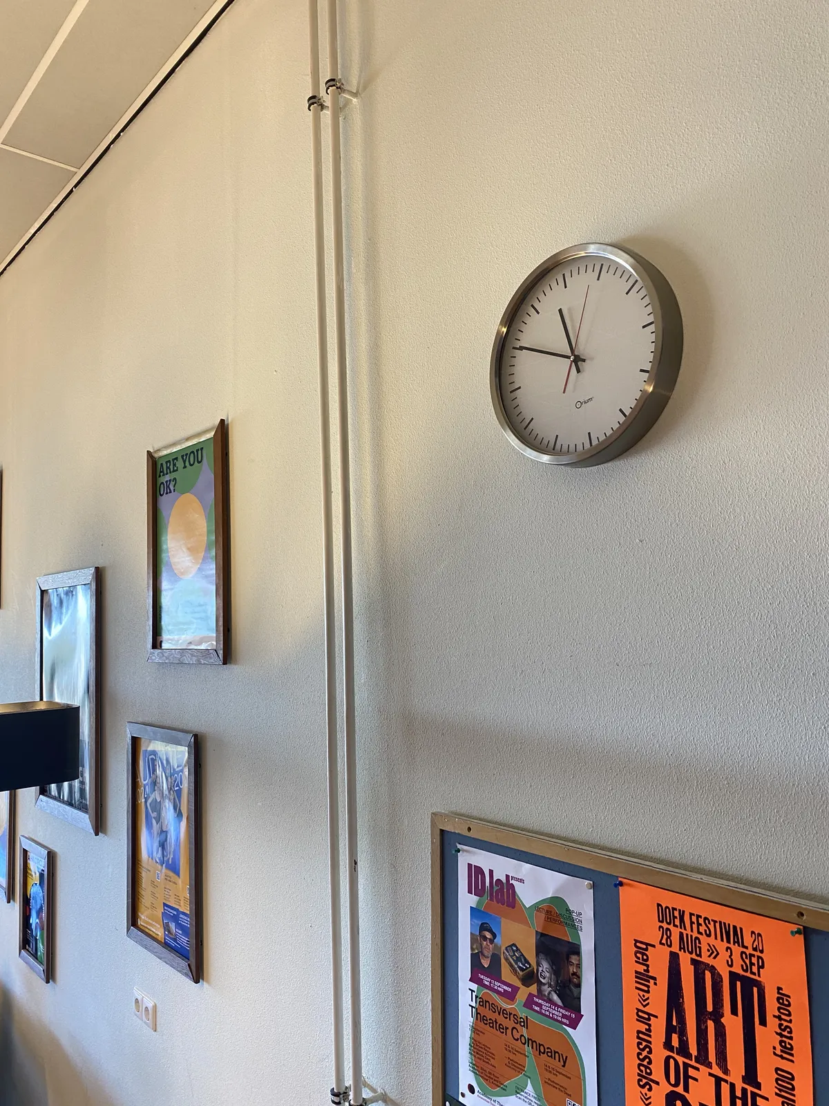 A clock on a wall. There are also some posters on the wall. The clock points at 10 to 12.