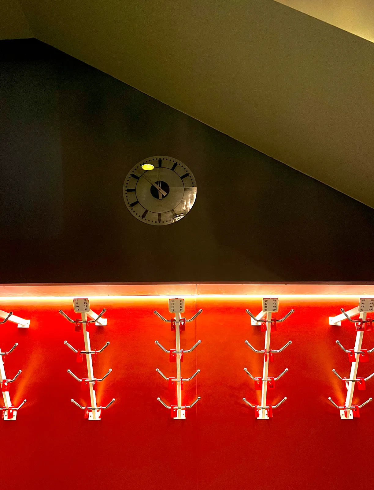 The lower half of this image is a red wall with metal coat hangers. The upper half is black with a clock that points at 8 minutes to 12.