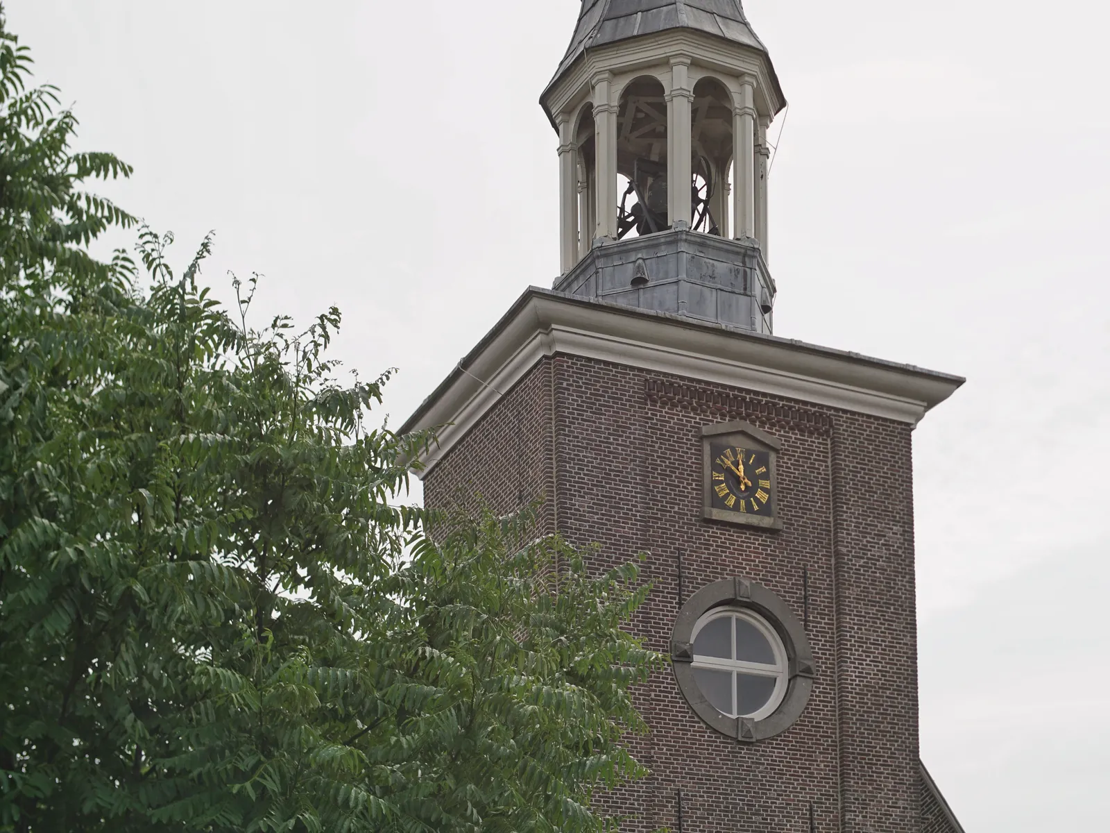 A tree and a church tower with a clock that points at 8 minutes to 12.