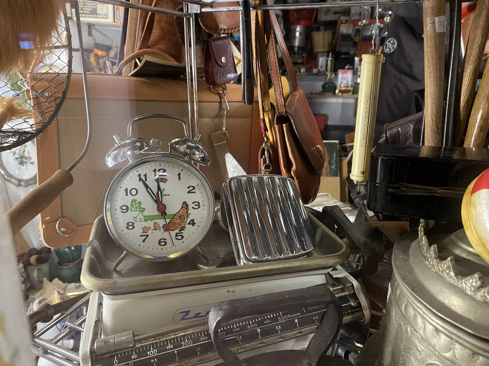 In a thrift shop there’s an old alarm clock, with bells on top and chicken printed in its face. It points at six minutes to twelve.