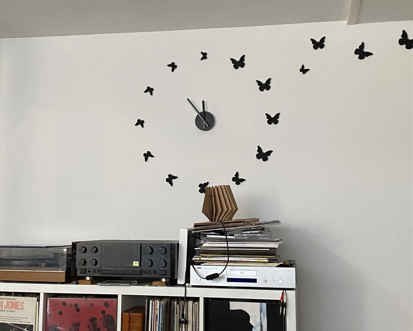 A clock on a wall, with black butterflies marking the hours, points at 6 minutes to 12.