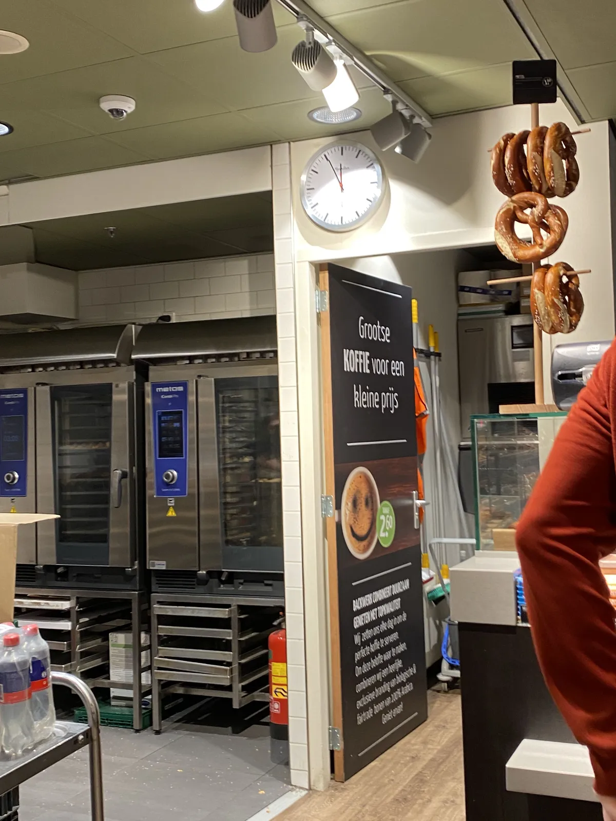 In a bakery there’s a clock hanging over a door. It points at 5 minutes to 12.