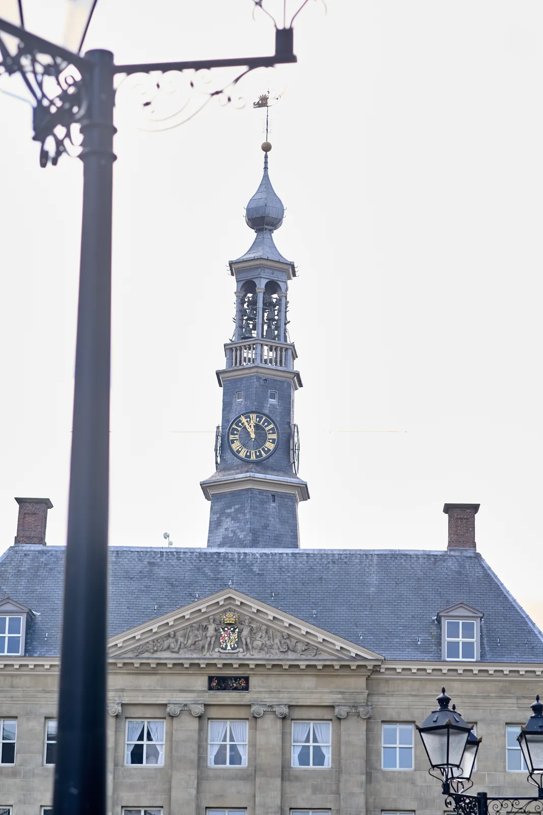 A large, ornamented church tower behind an old building. It looks like a town hall of a wealthy old Dutch city. The clock on the tower points at 5 to twelve.