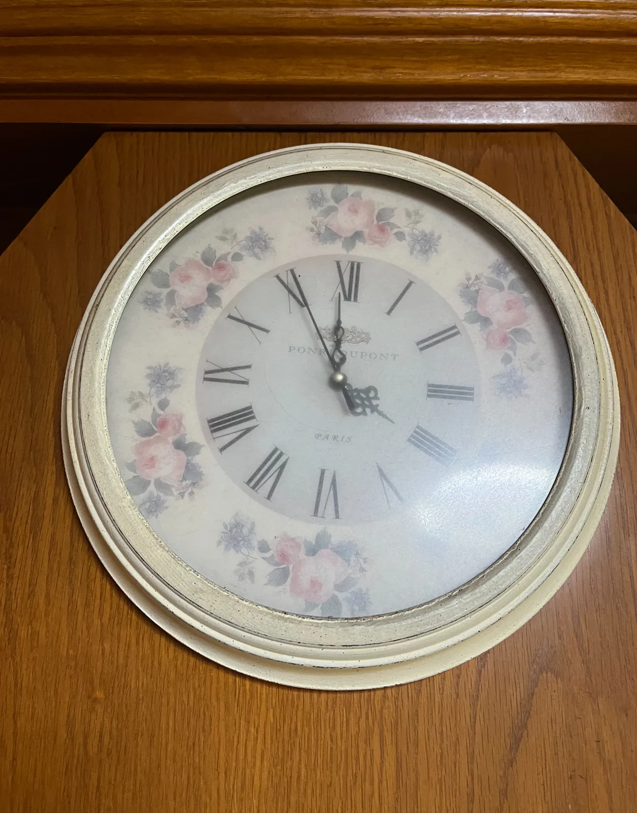 A pastel coloured clock with some flowers on its face. It points at 5 minutes to 12.