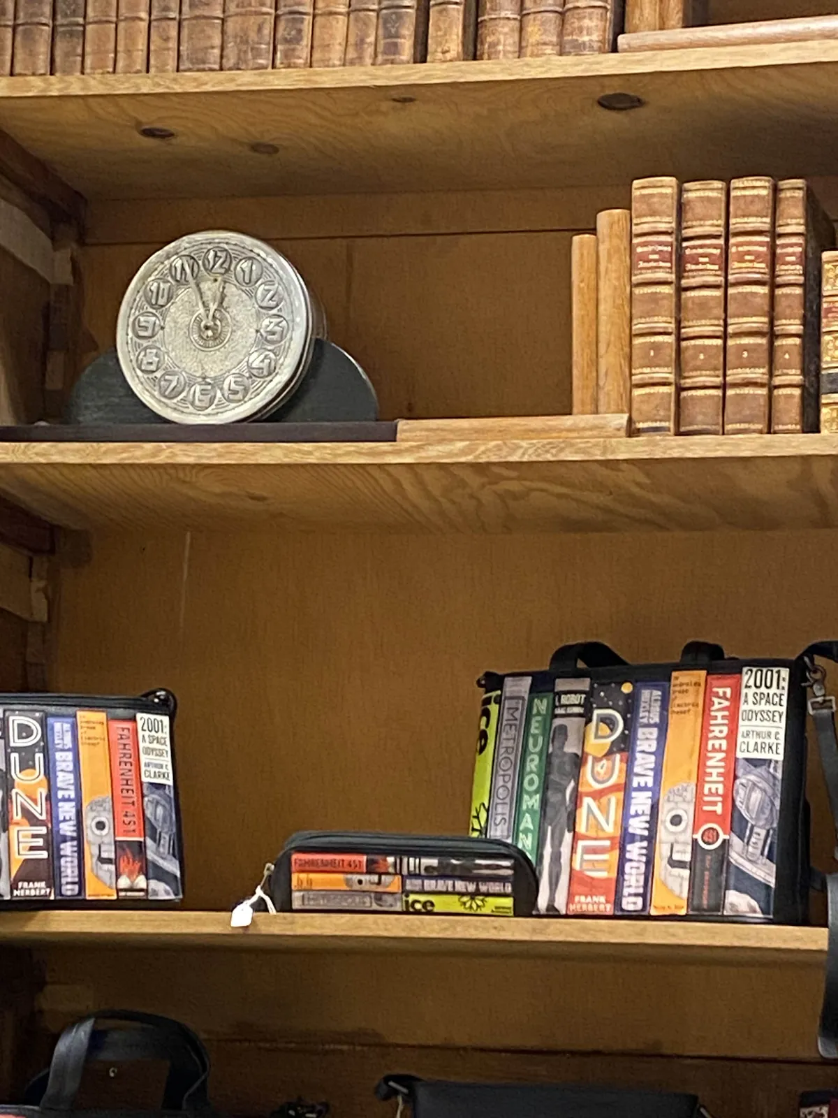 A bookcase. There are some very old looking books, they could also be props, it is not entirely clear. Then there are some science fiction books, which turn out to be the spines printed on a bag. It turns out there are three different science fiction book bags in this image. There’s also a clock which points at 5 minutes to 12.