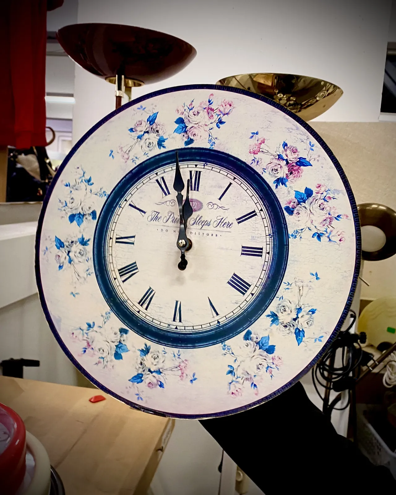 A clock with lots of flowers on it points at 2 minutes to 12.