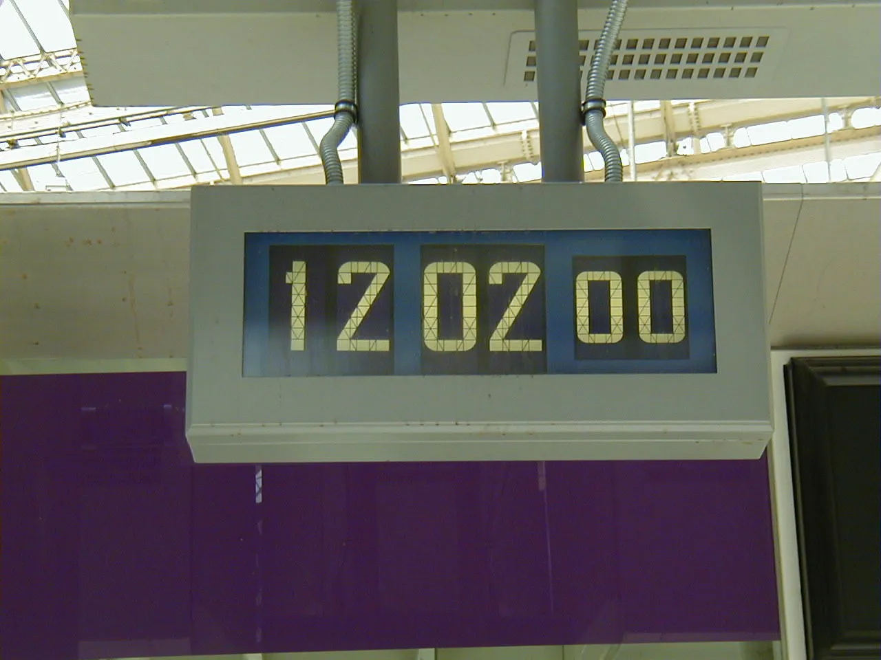 This large clock, hanging from a ceiling, says it is 12:02