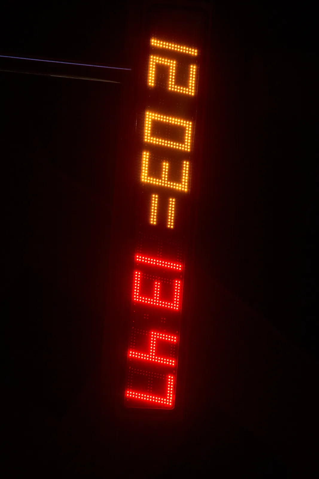 A digital display with segmented numbers on it. They form two different time stamps. According to the orange time stamp it is 3 minutes past 12, and according to the red time stamp it is 13 minutes to two.