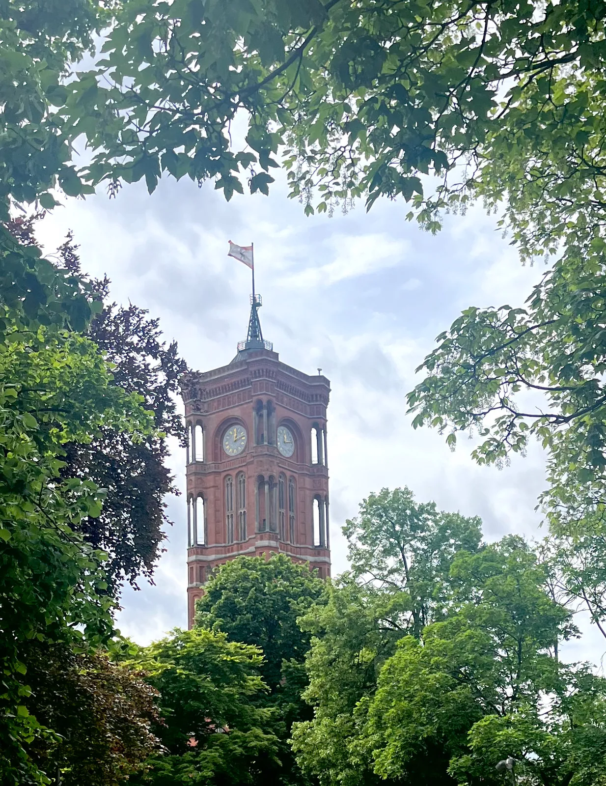 Peeking through the trees. There’s a tower with a clock on it that points at 12 minutes past 12.