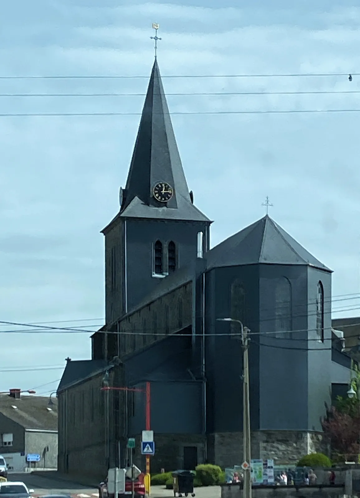A black church with a clock on its tower. It points at a fourteen minutes past twelve.