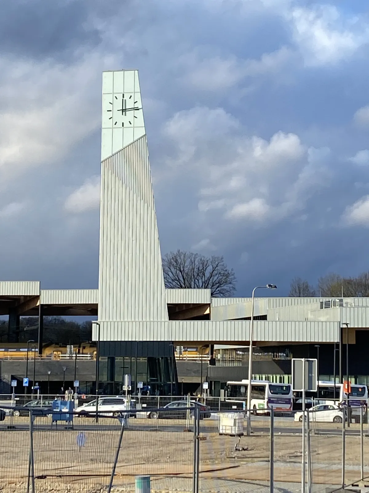 A high tower on a building. The building and the tower form an abstract composition. On the towser there’s a clock which points at 14 minutes past 12.