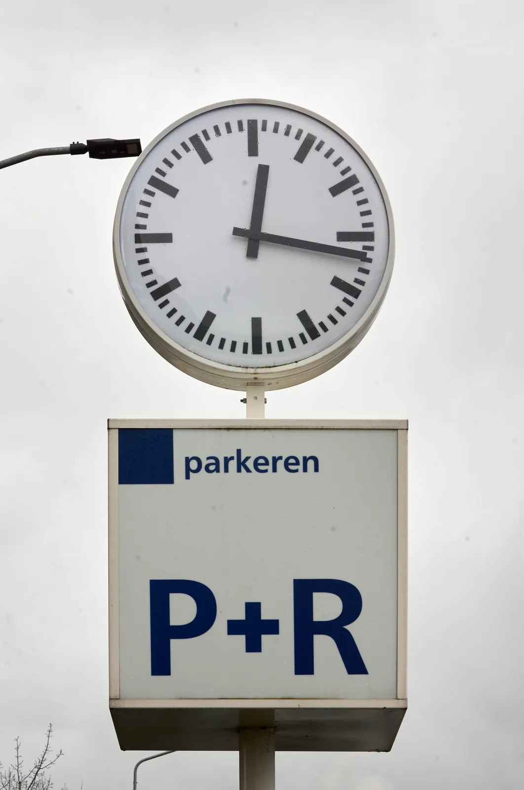 A clock on top of a parking sign points at 16 past twelve.