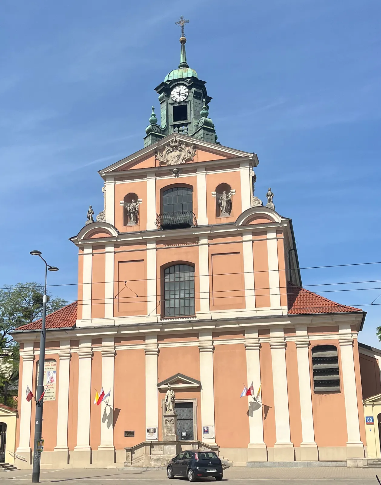 A sunny day. An old orange church with a clock. It points at 18 minutes past 12.
