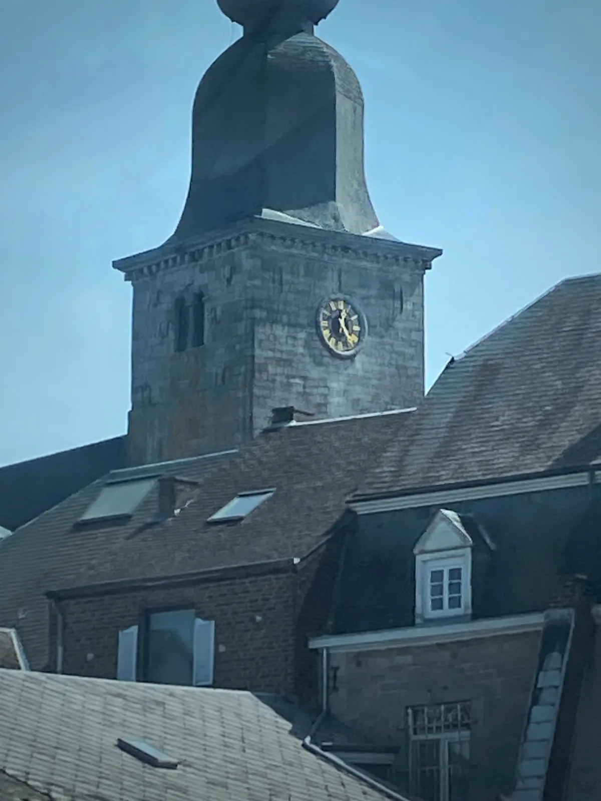 A landscape of roofs, with a bulbous church tower in the beck. It has a clock on it that points at 24 minutes past 12.