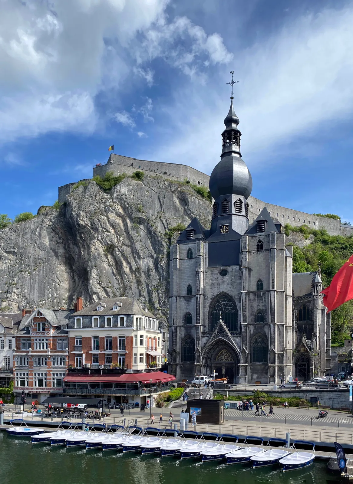 An old church with a rather strange bulbous tower. Behind it is a massive cliff, and in front of it there’s a little harbor. The clock on the church points at 27 minutes past 12.