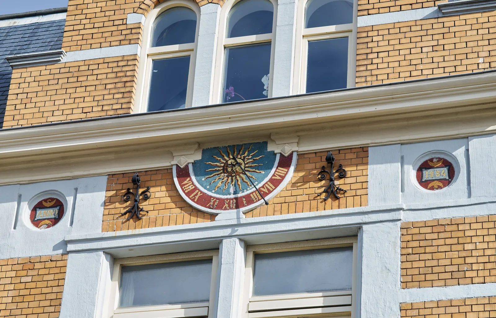 It says Anno 1884 next to this sundial, with a mosaic of the sun on it. It points at approximately 12:30.