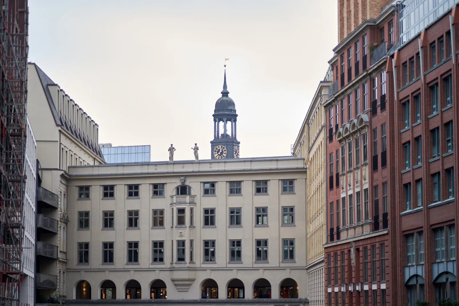 A Hamburg cityscape with a church tower peeking over an old office building. The clock on the tower points at 21 minutes to one. 