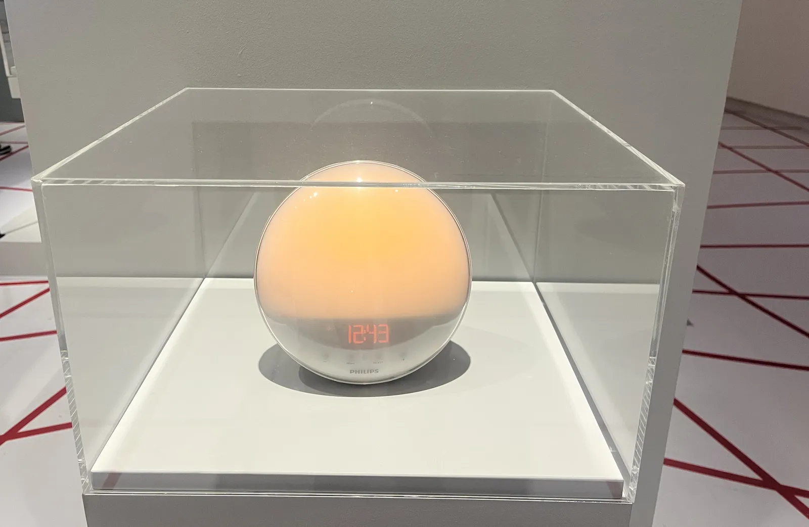 A sphere, made by Philips, in a glass showcase. It emits a yellow light, and it displays the time as 12:43