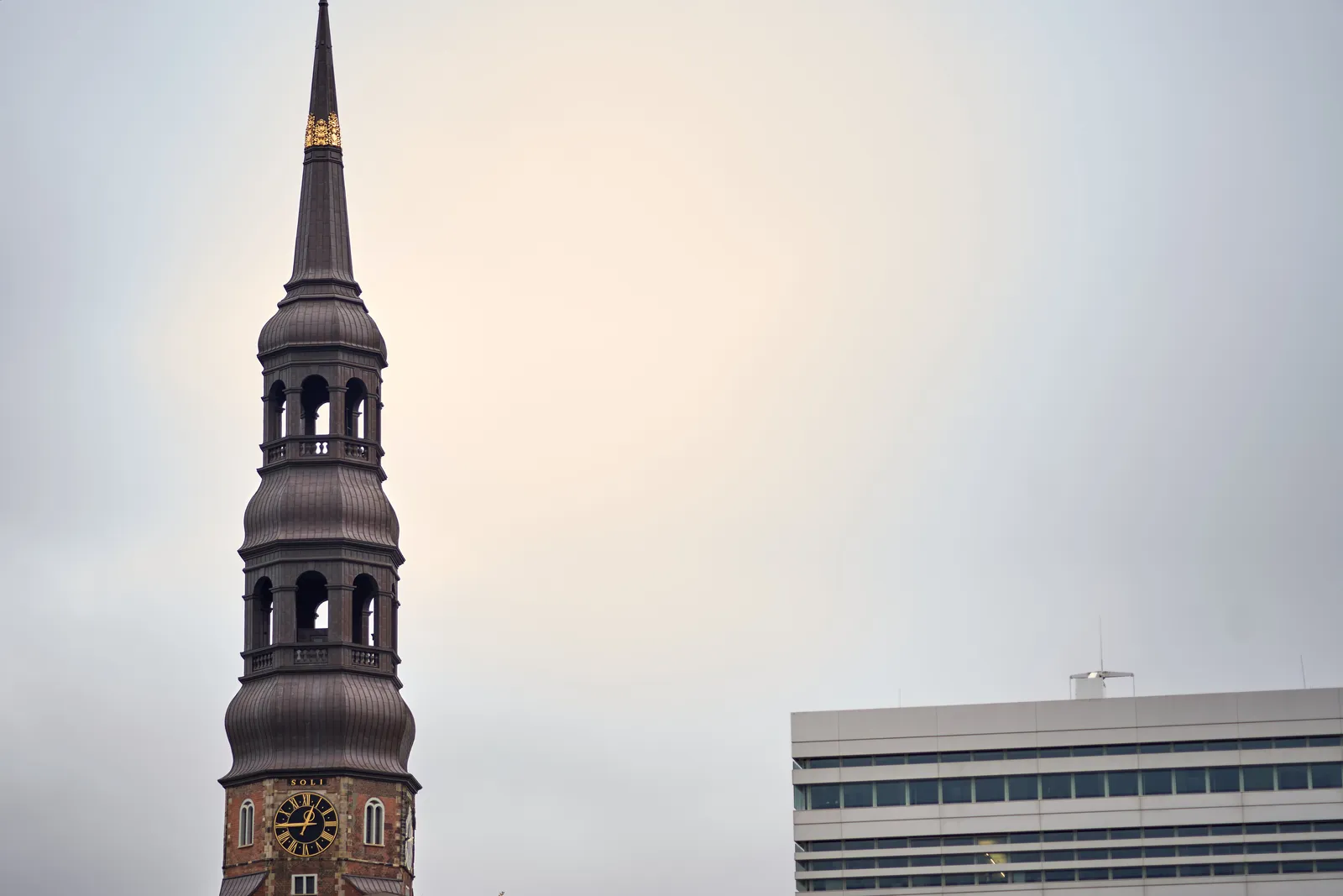 Next to a rather boring modernist building there’s a high pointy church tower with a clock that points at a quarter to one.