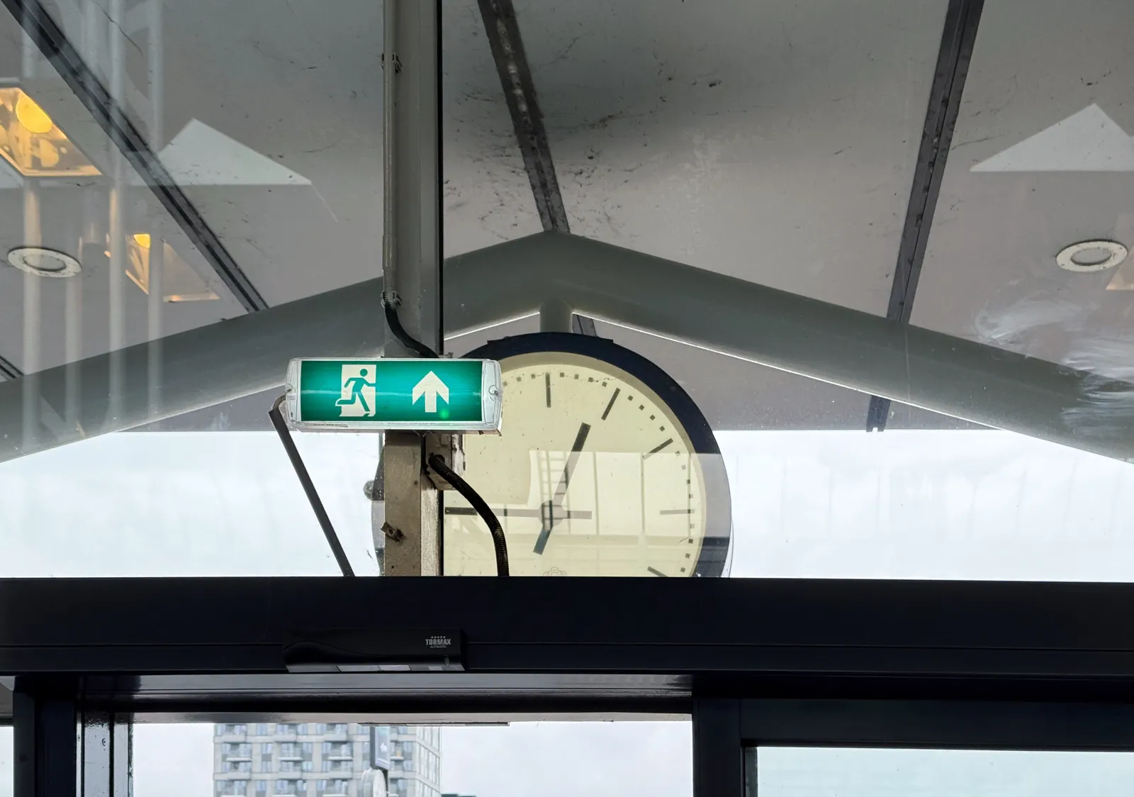 Peeking out, through the window of a train station in the Netherlands, at a clock that seems to point at a quarter to one.