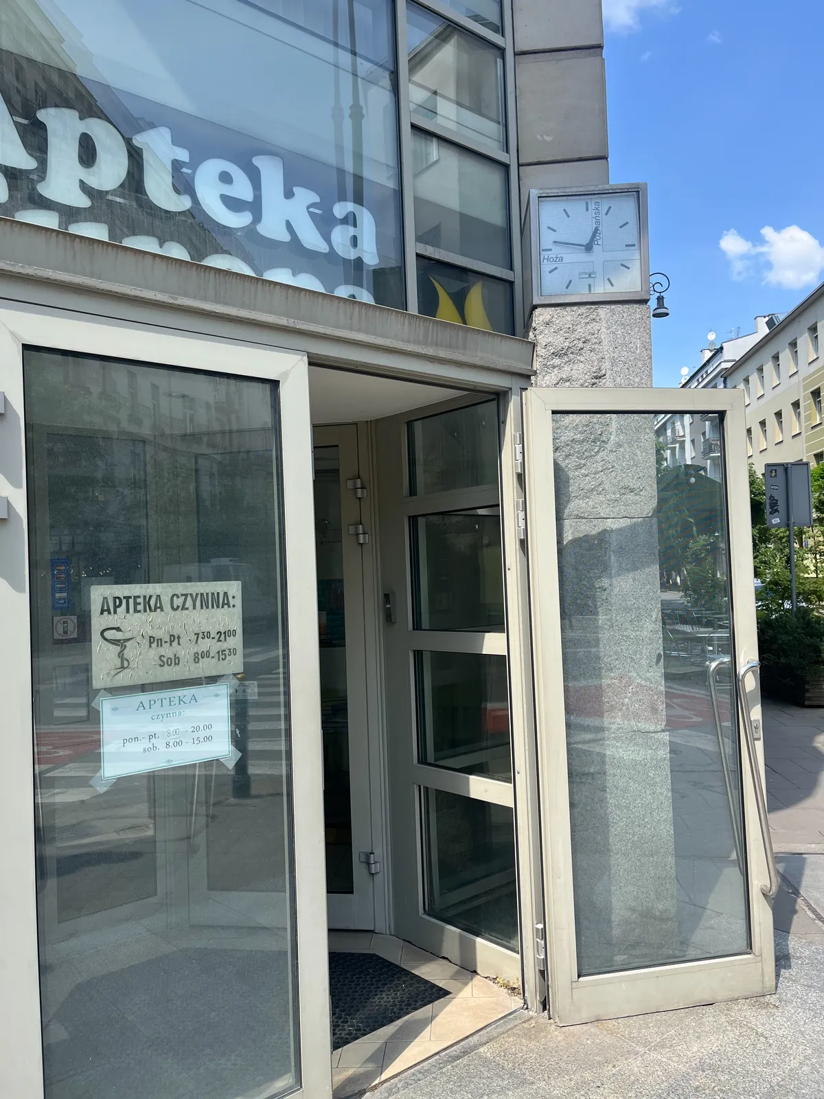 A clock next to a door on the corner of a street. It points at 13 minutes to one.