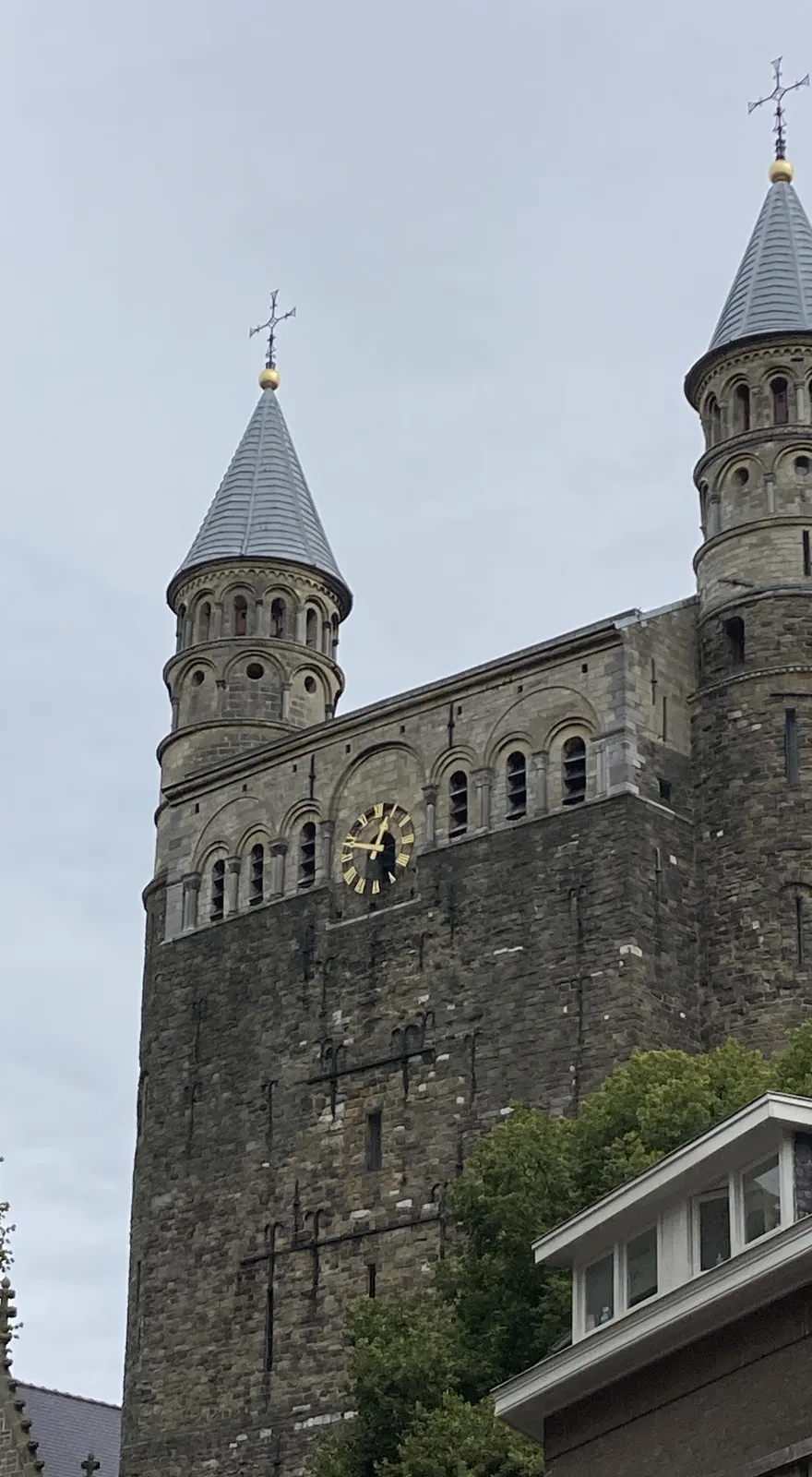 A building that looks like a high, medieval castle, The upper part on this building, the part with the towers seems to be a bit newer. There’s a golden clock on the wall, and it points at 11 minutes to one.