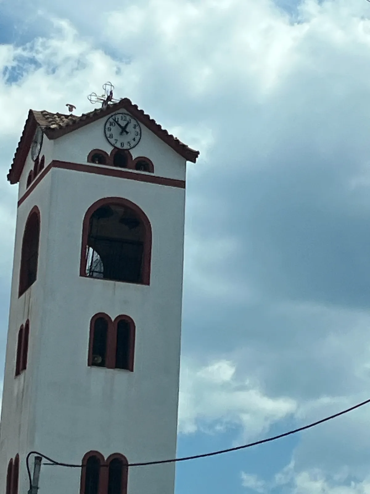 A clock on top of a simple, white and red church tower. It points at 7 minutes to one.