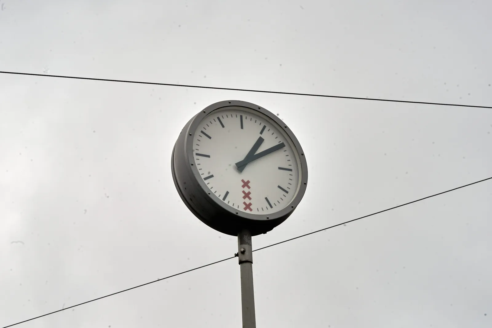 A clock from the municipality of Amsterdam, mounted on a pole, points at ten past one. 