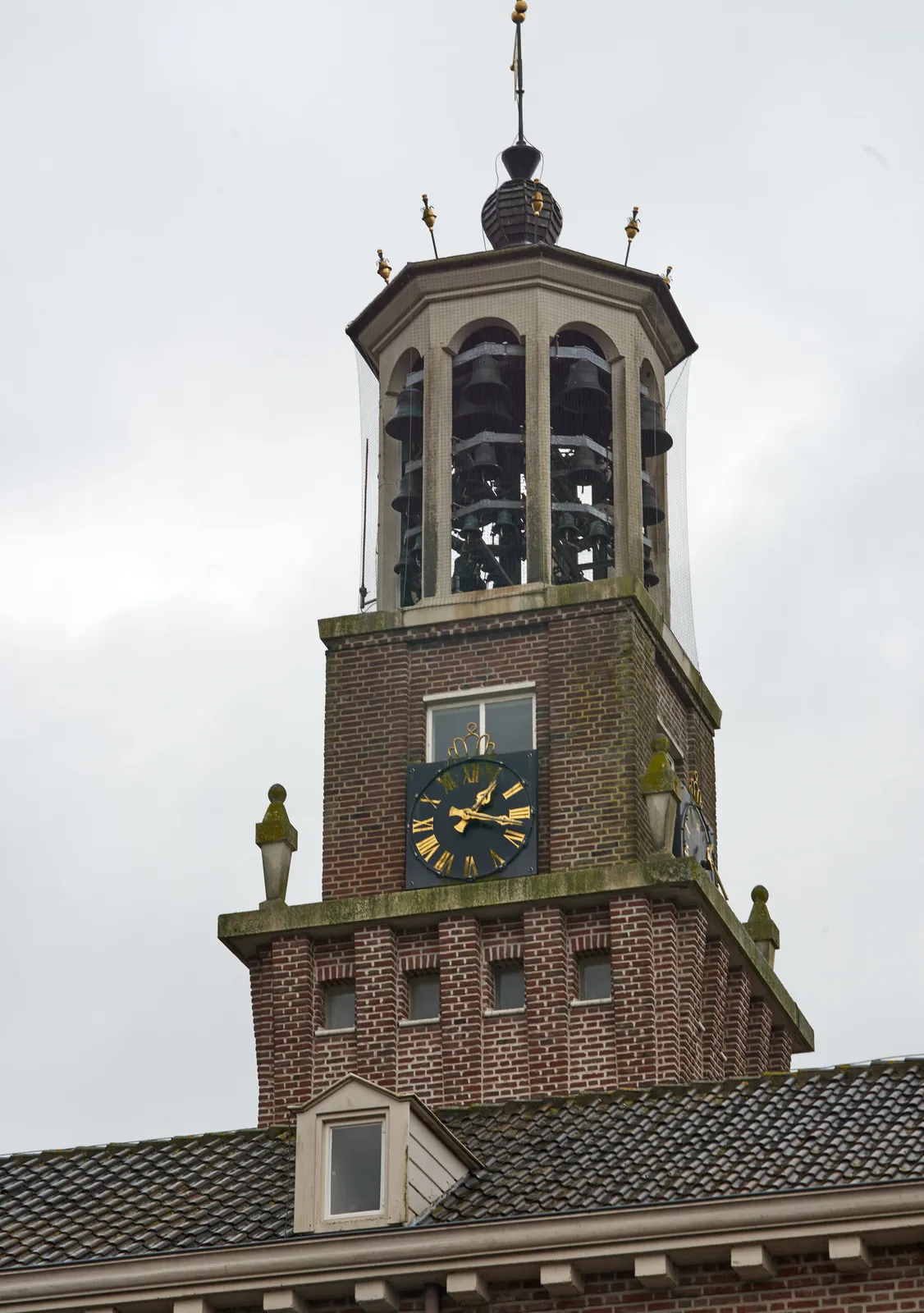 There are many, many bells in this old tower. Below the bells there’s a clock that points at 17 past one.