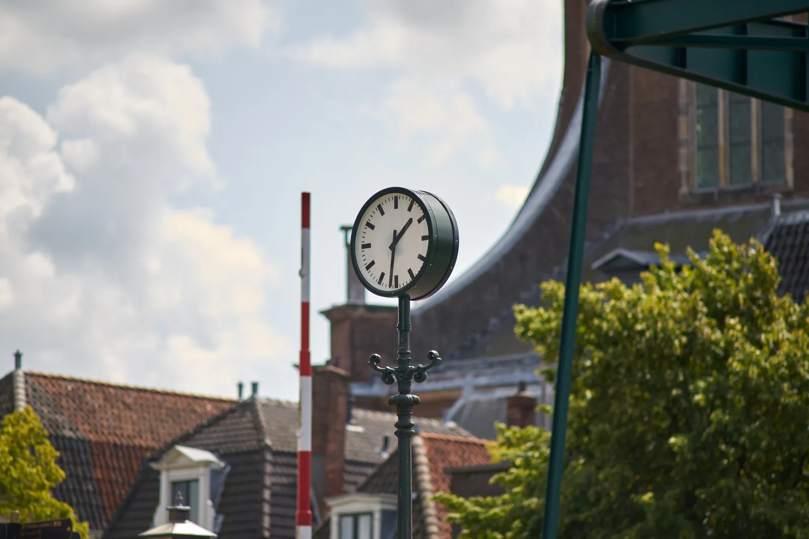 A clock on a pole in a city landscape. It points at 31 past one.