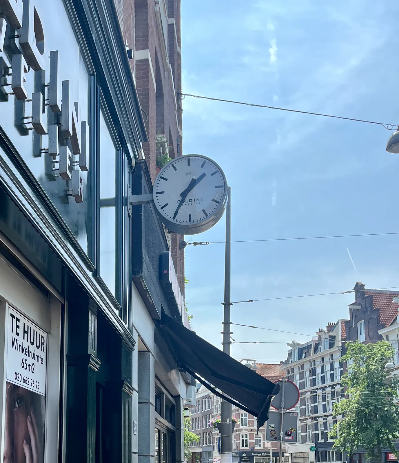 On a bright sunny day, a clock attached to facade in a shopping street in Amsterdam points at 35 minutes past 1. 