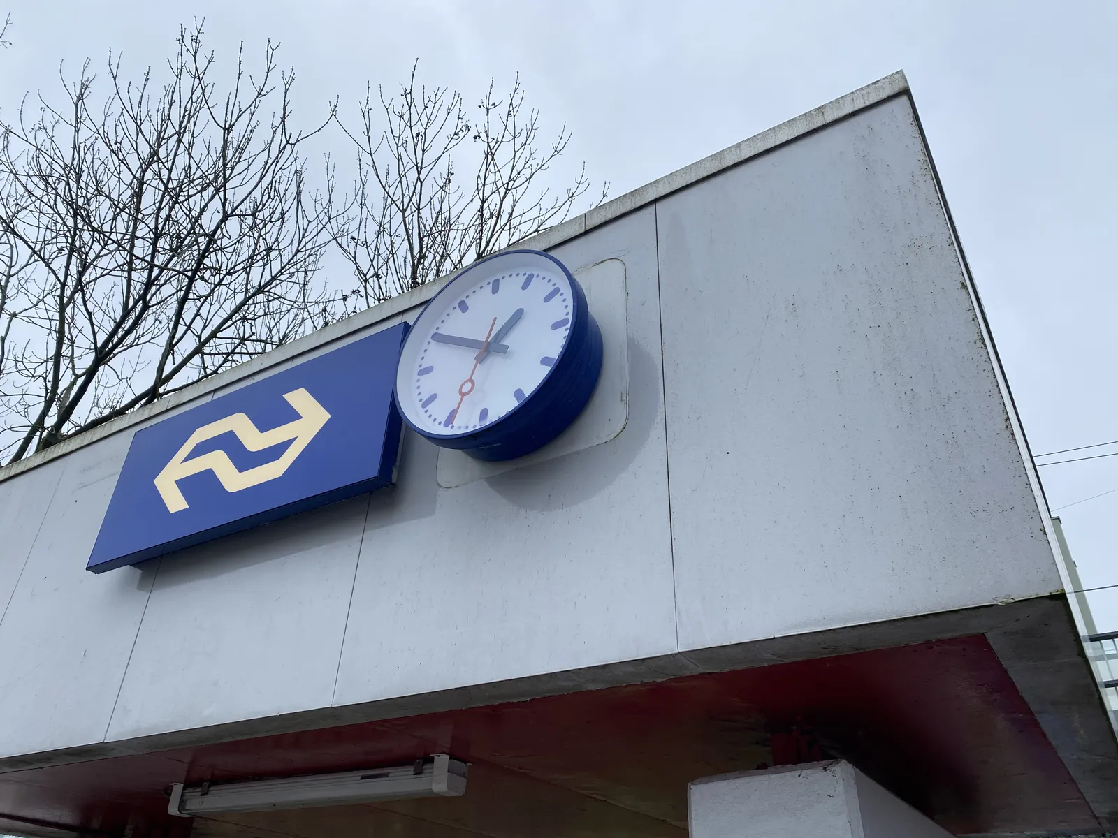 A clock attached to the facade, next to the famous logo of the Dutch railways. It points at 10 minutes to 2.