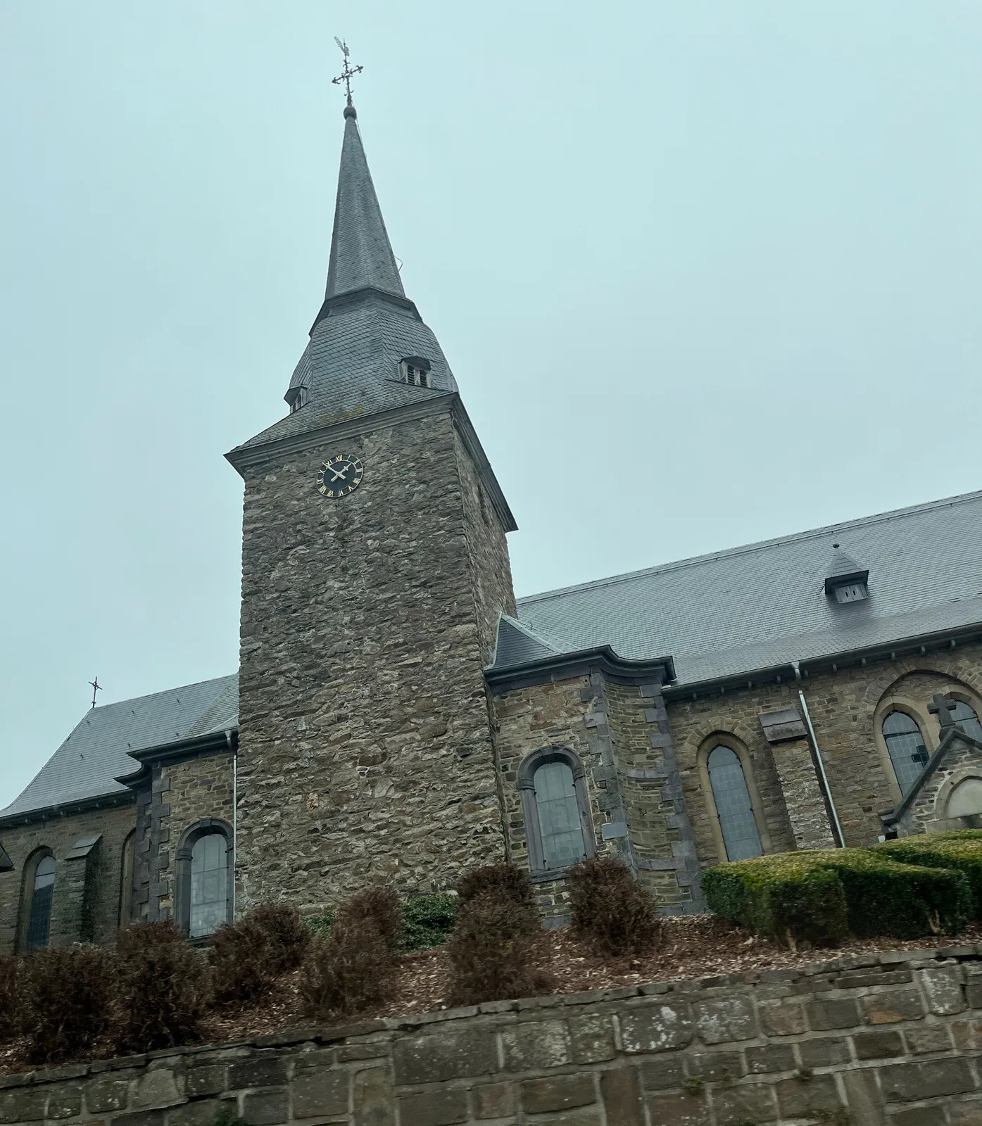An old, large, grey, stone church, with a relatively small clock on it. It points at 6 minutes to 2.