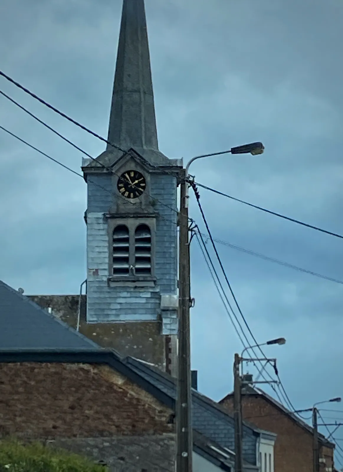 Streets lamps with wires between them. In the background there’s a church with a clock that points at 5 minutes to 2.