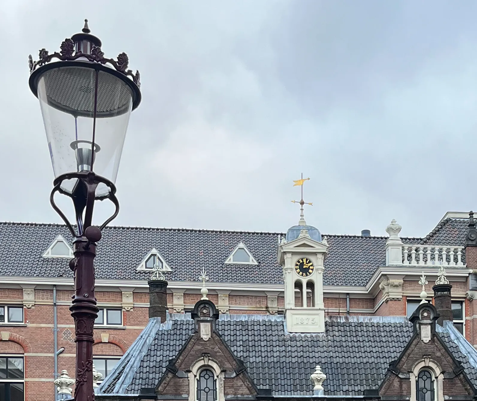 A clock on a little tower on top of an old building in Amsterdam. It points at one minute past 2.