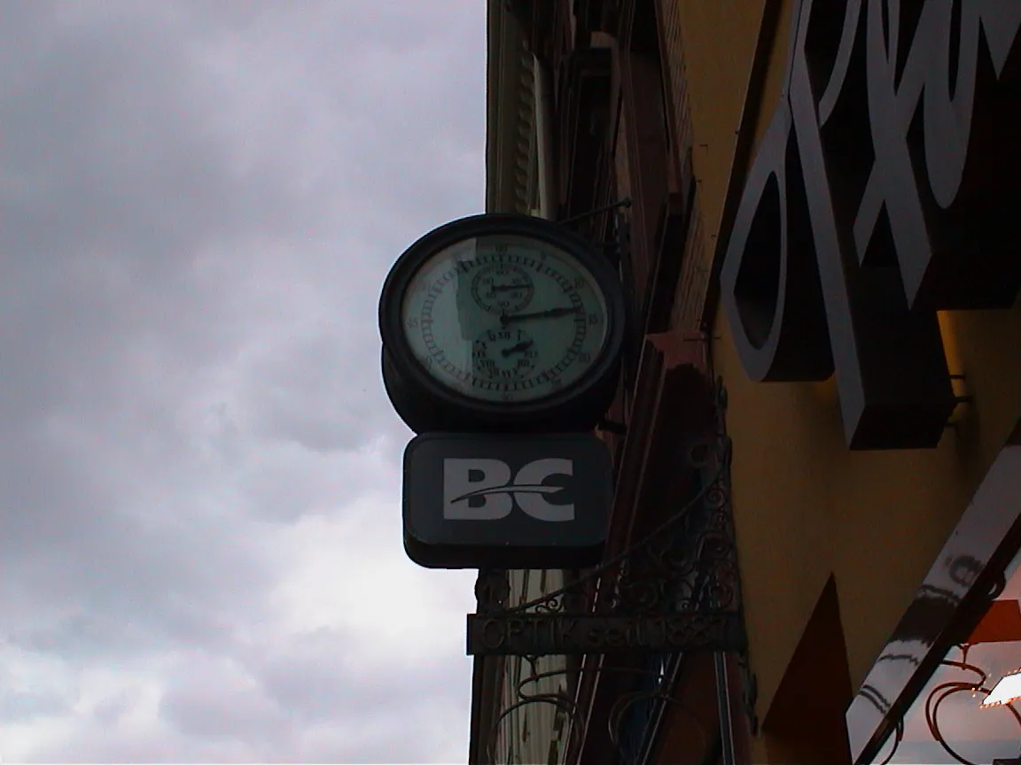 This clock attached to a building points at thirteen minutes past two.