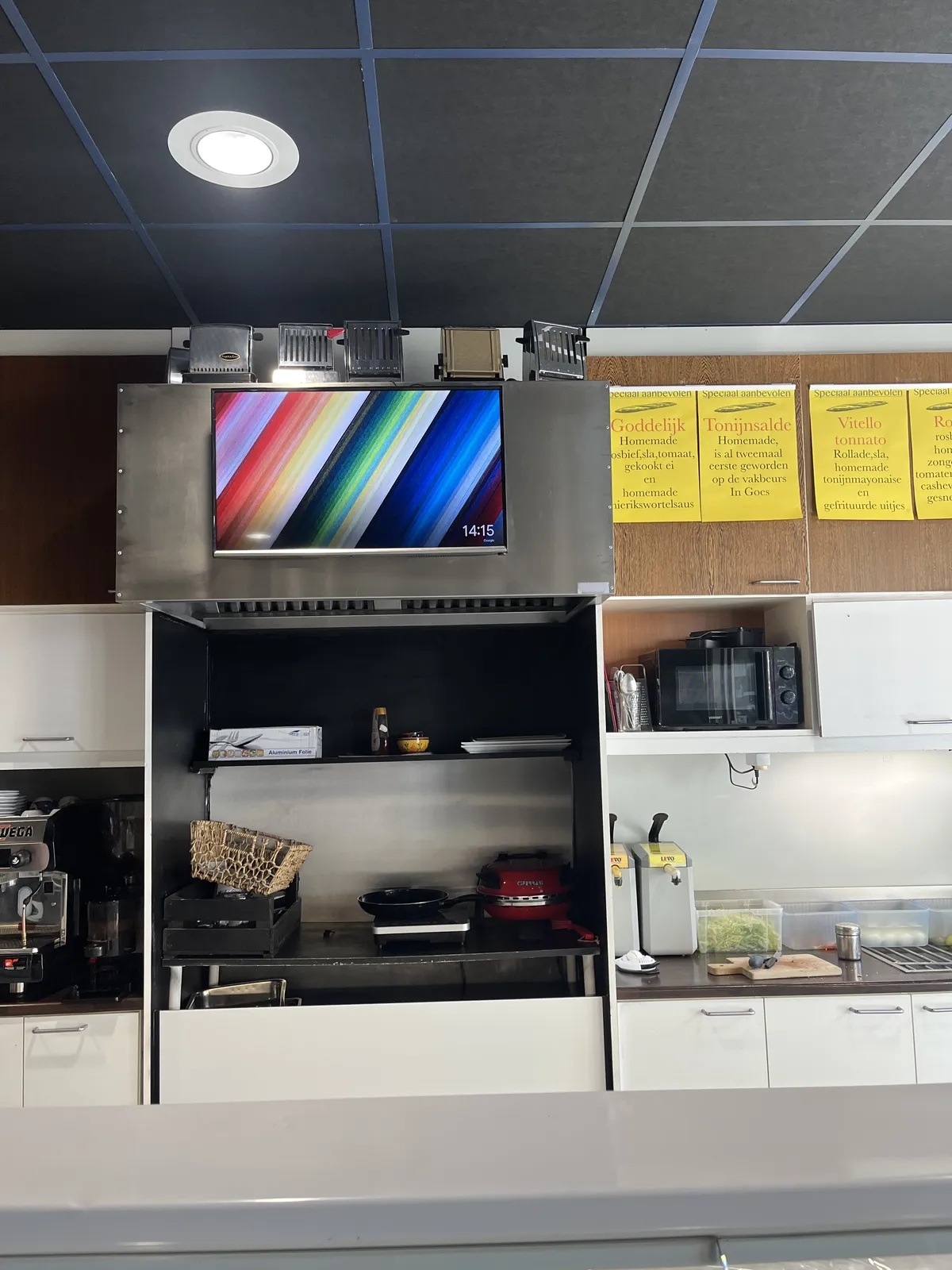 In a sandwich shop, between the cupboards, and below quite a few old fashioned toasters, is this colourful display which shows the time in the bottom right corner as 14:15