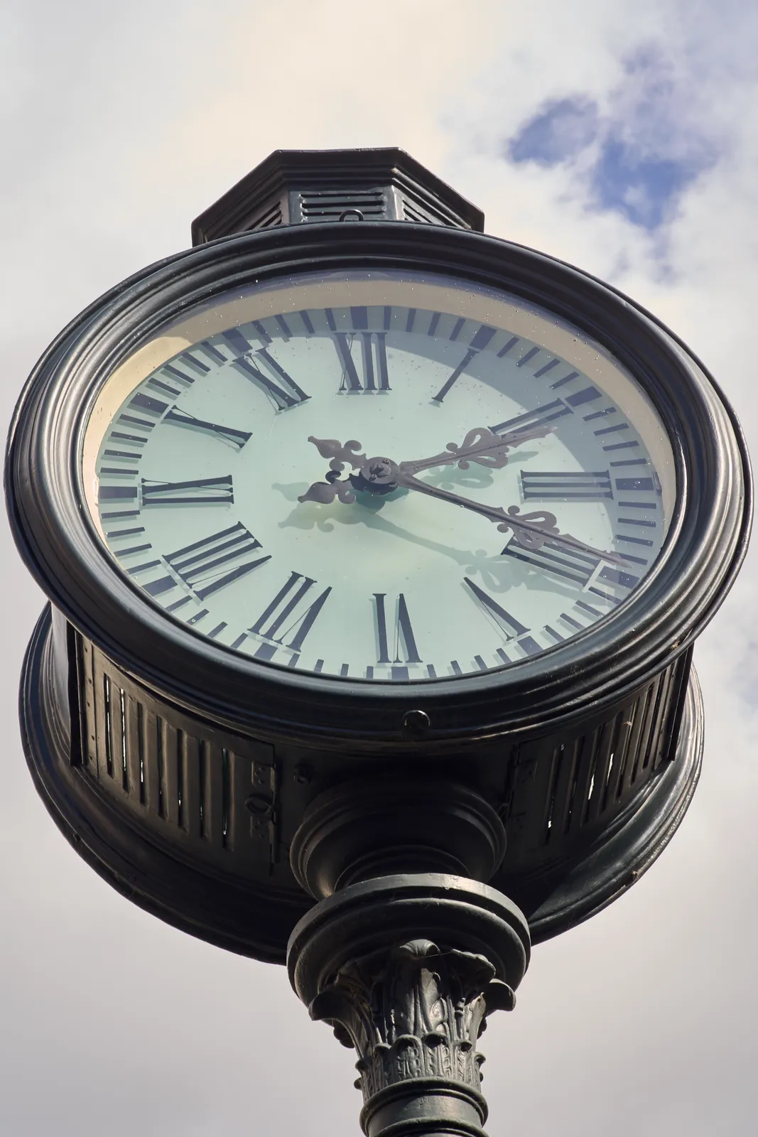 A neoclassical black clock on a pole. It points at 19 minutes past two.
