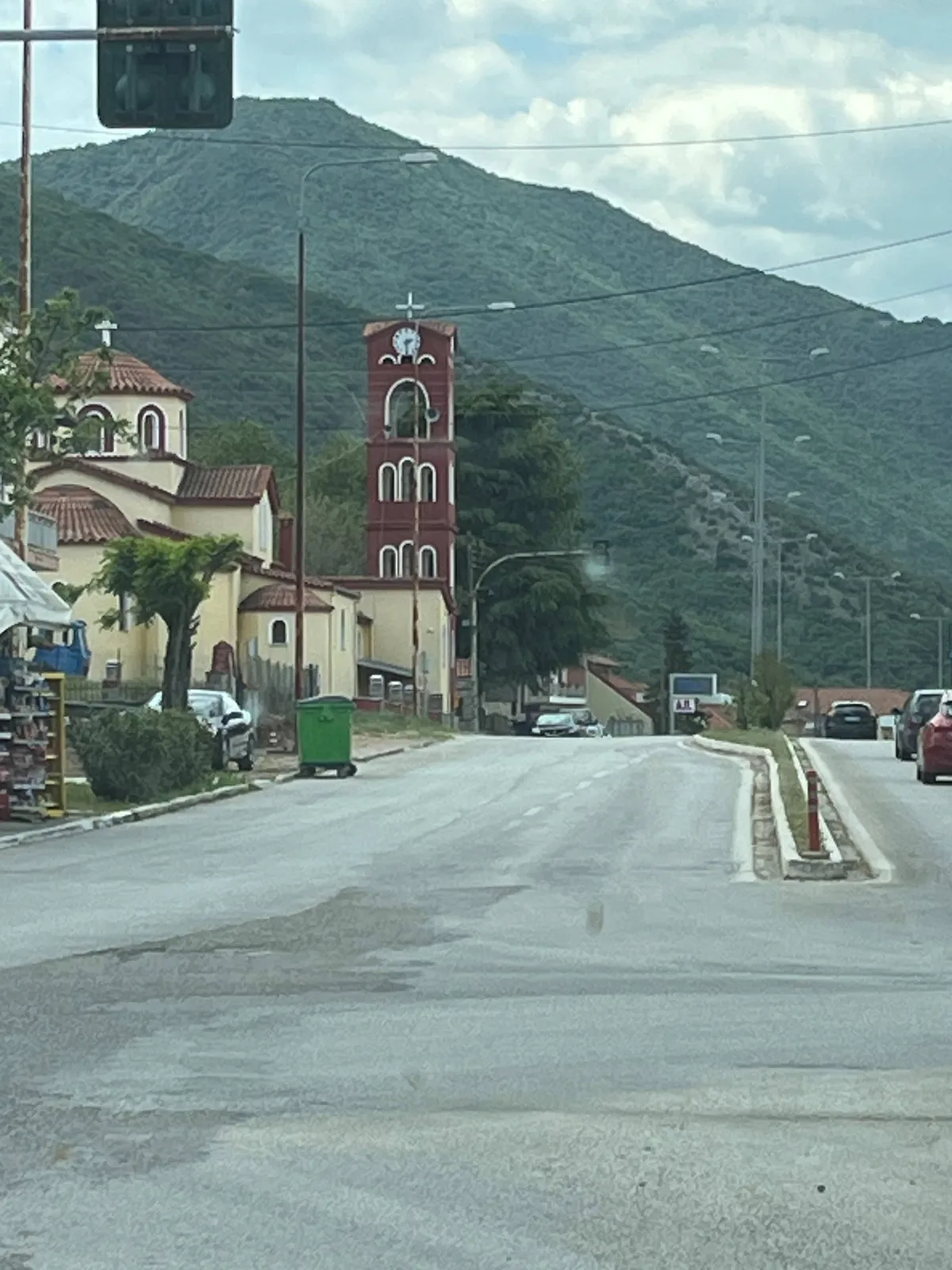 A simple red church tower in the background, with large green mountains behind it. The clock points at half past two.