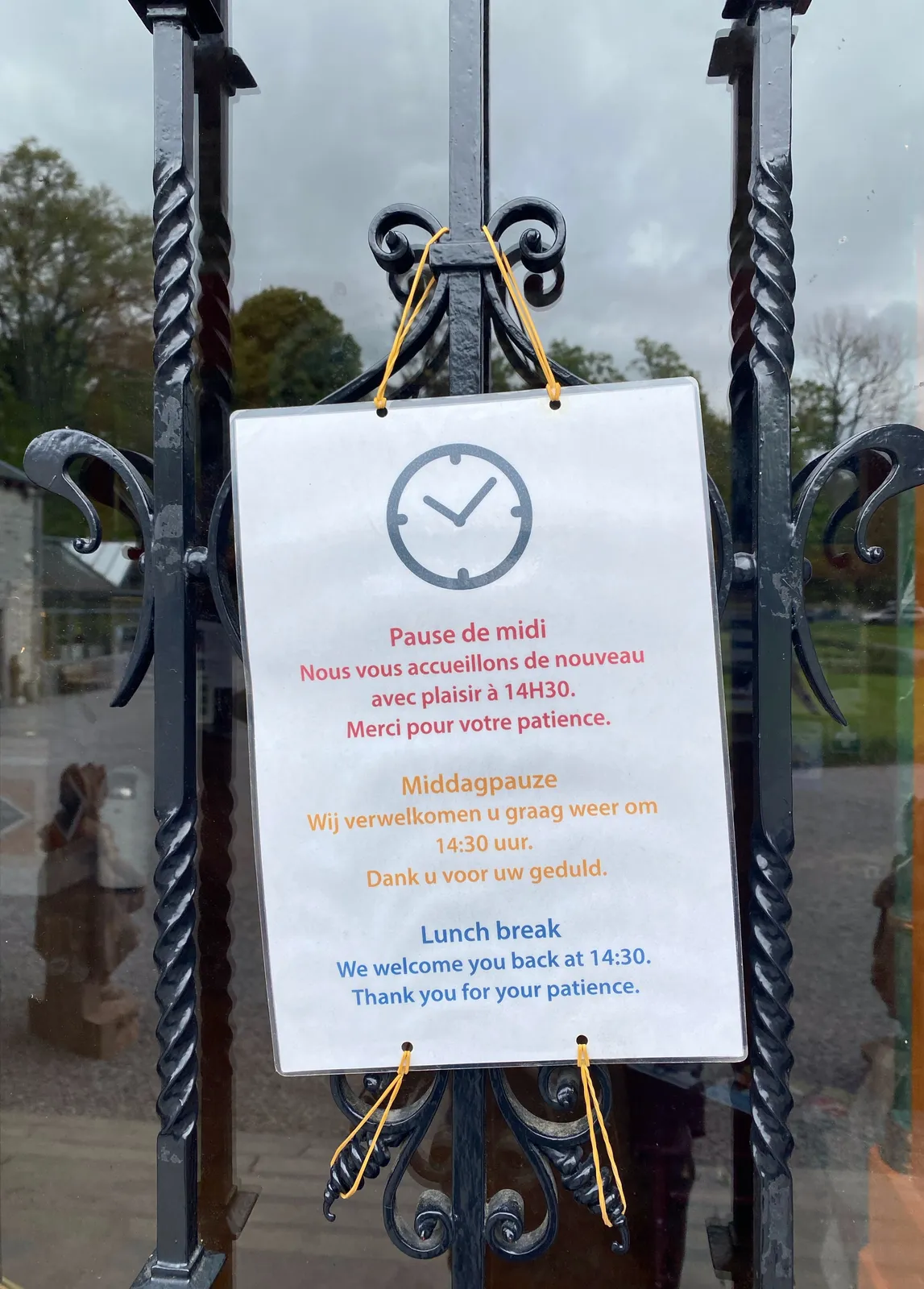 A simple sign attached to a door says, in French, in Dutch and in English that lunch break is over at 14:30. There’s an image of a clock on the sign which points at 9 minutes past 10.