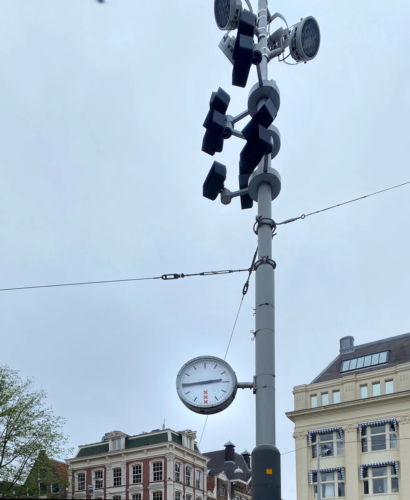 Some old houses in the background, and a pole with lights and a clock attached to it in the foreground. The clock points at 18 minutes to 3.