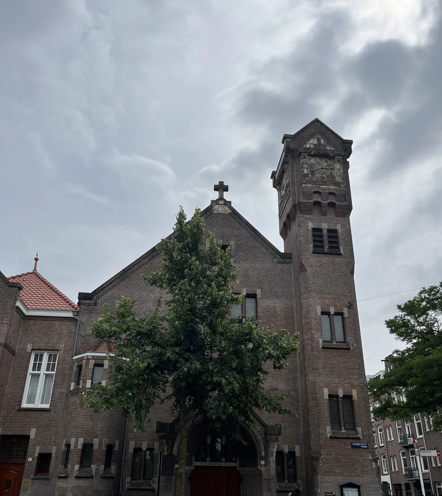 A brick building, which seems to be a church. On the tower there’s a clock. The hands are the same colour as the face, so it’s very hard to see what time it is exactly. But when you look closely you can see that it is 18 minutes to three.