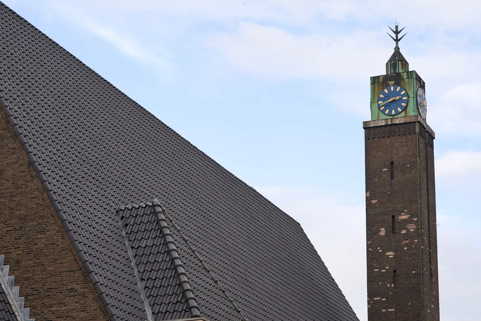 A big roof of a church, and a church tower with a clock. It points at 18 minutes to 3.