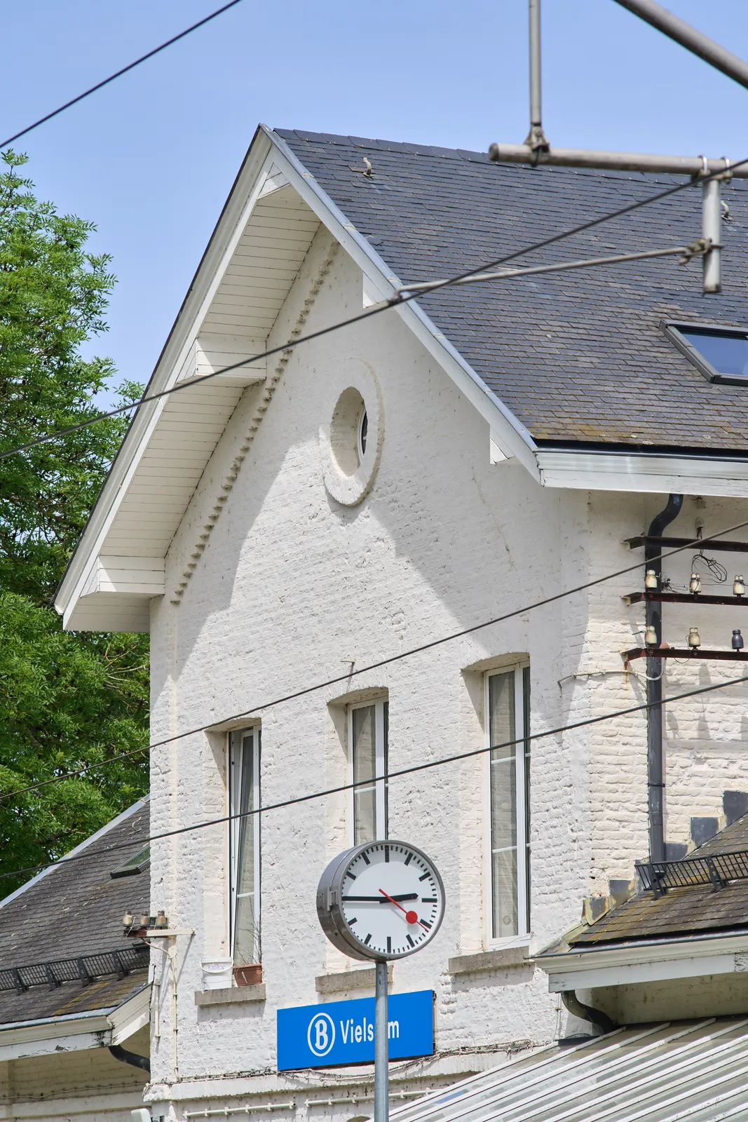 In front of the white brick building of the Vielsalm train station, there’s a clock on a pole. It points at a quarter to three.