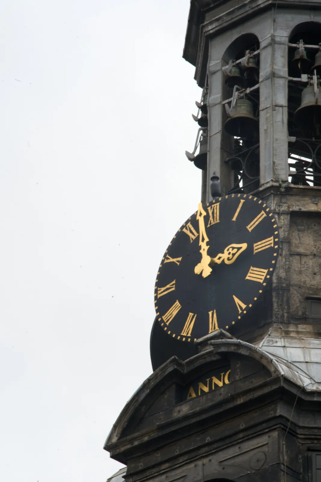 A detail of an old tower. It says Anno on it, but the year is outside of the frame. There’s a black clock with golden roman numerals, and golden hands on this tower. It points at 2 minutes to 3.   