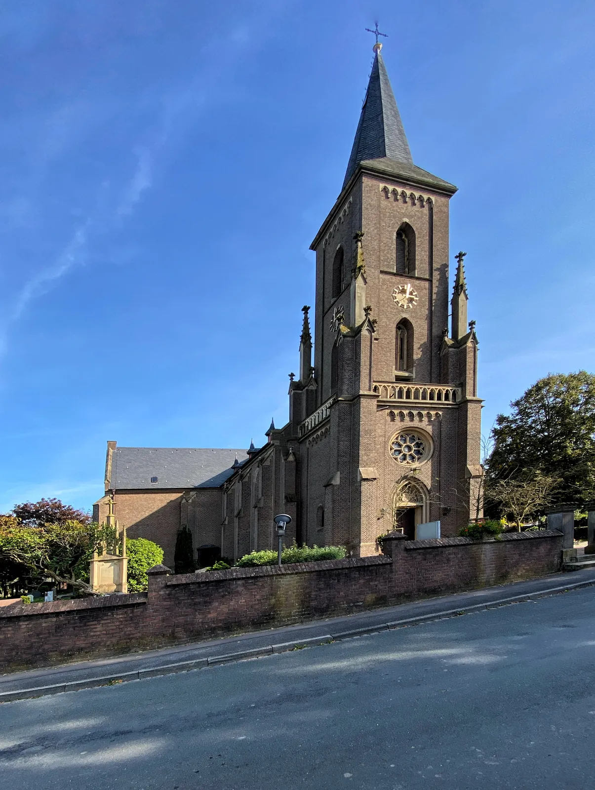 A brick church standing straight, at a downhill road. The clock on the church points at 2 minutes past 3. 