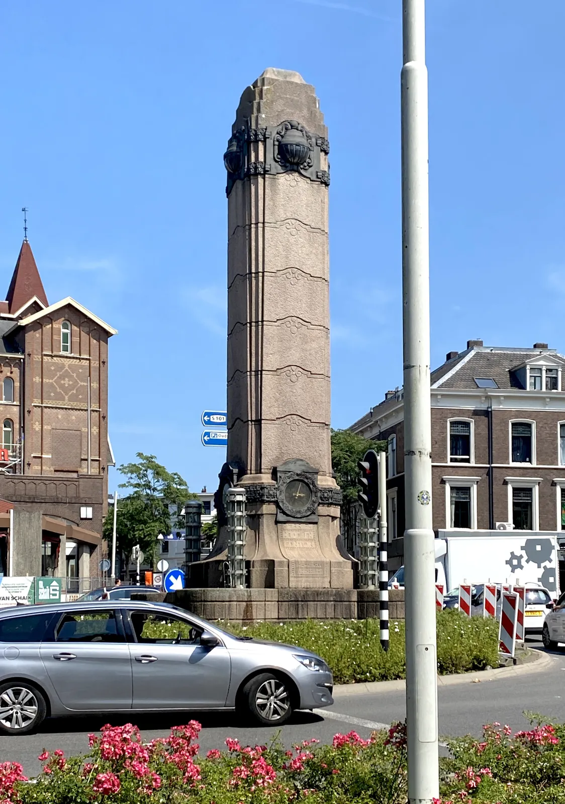 A very large, monument, shaped like a phallus, on a roundabout. There’s a clock on this erect column, which points at 5 past 3.