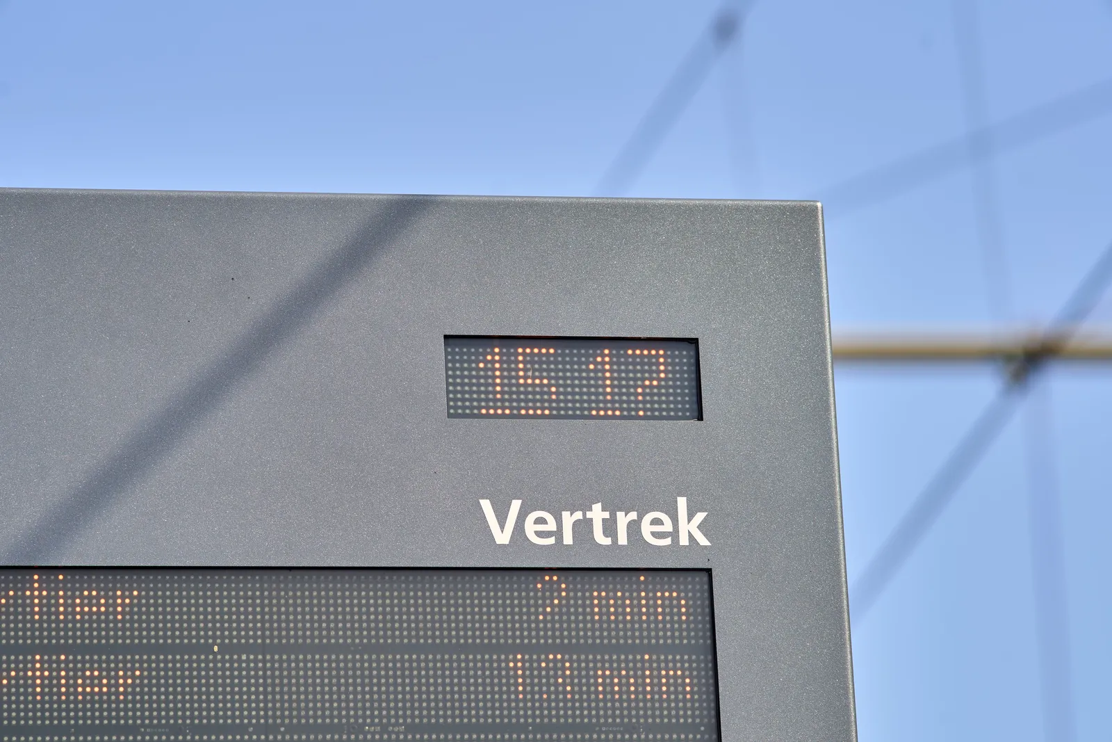 It’s a bright sunny day. There’s a part of a display that shows the time that trams leave. It also shows the time as 15:17.  