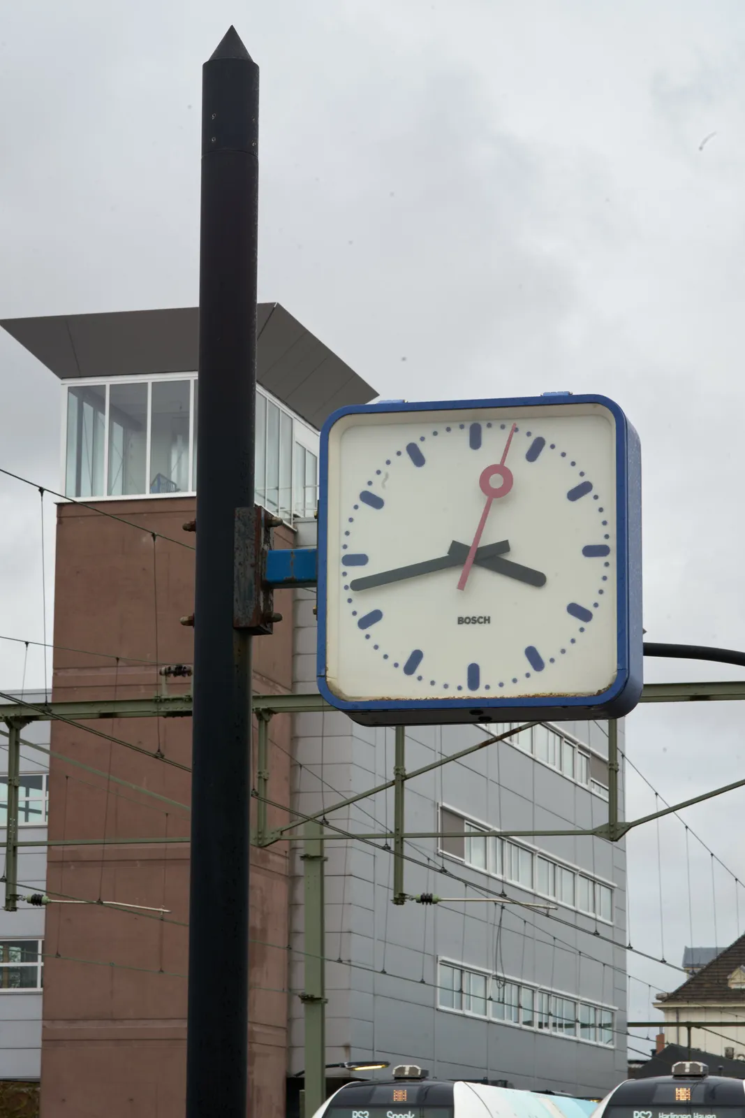 A clock attached to a pole points at 17 minutes to 4.