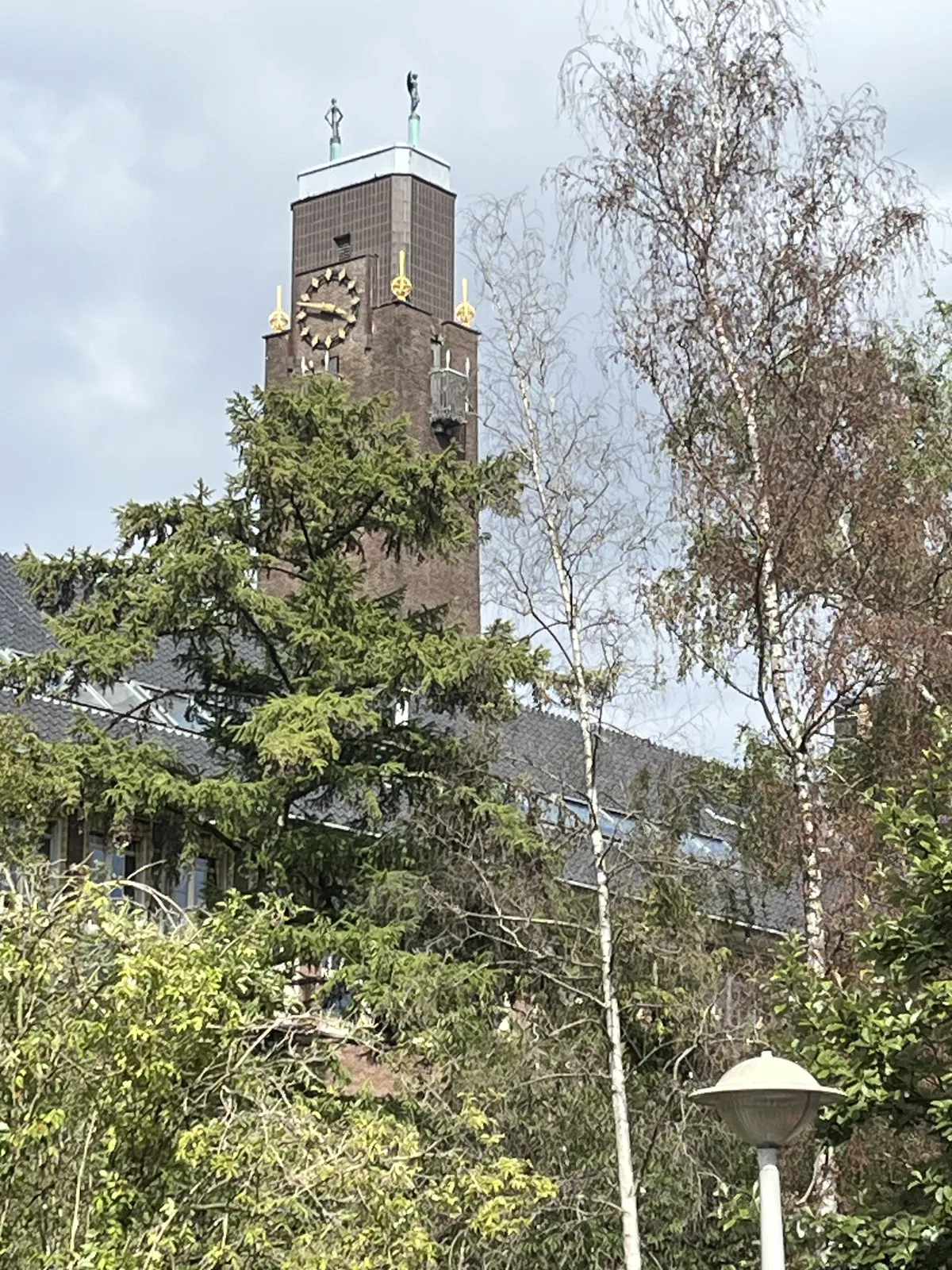 Trees in the foreground, and a eye catching tower, with golden ornaments, and two statues of skinny, cheering figures on top. There’s also a clock on this tower, which points at 12 minutes to four.
